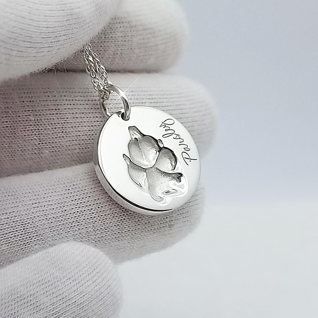 Silberne Halskette mit rundem Anhänger, eingravierte Pfote und Name Pandora, gehalten mit weißem Handschuh
