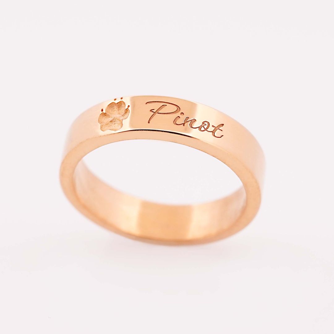 Detailaufnahme eines goldenen Rings mit Gravur Pinot und einer Pfote, vor weißem Hintergrund