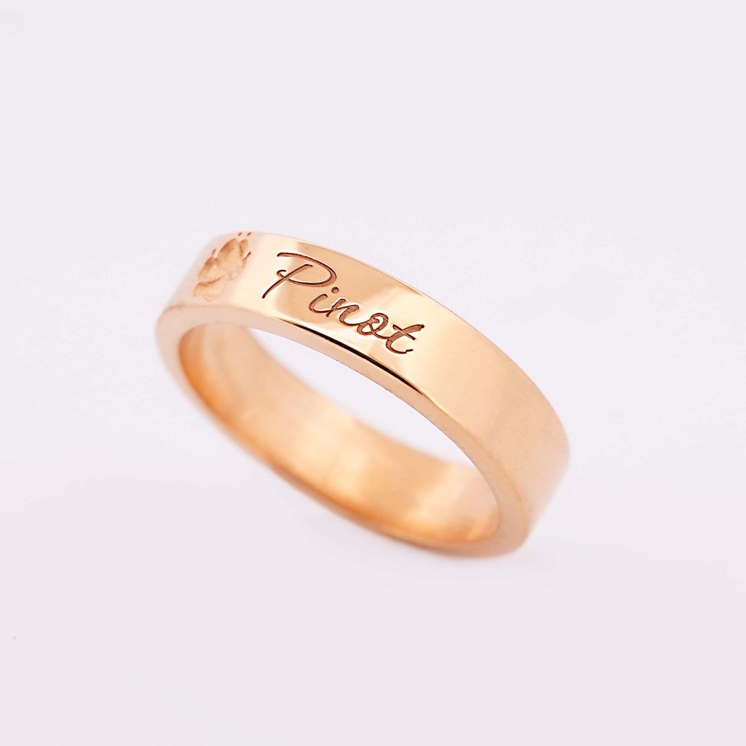 Goldener Ring mit eingraviertem Namen Pinot und kleiner Pfote, vor hellem Hintergrund