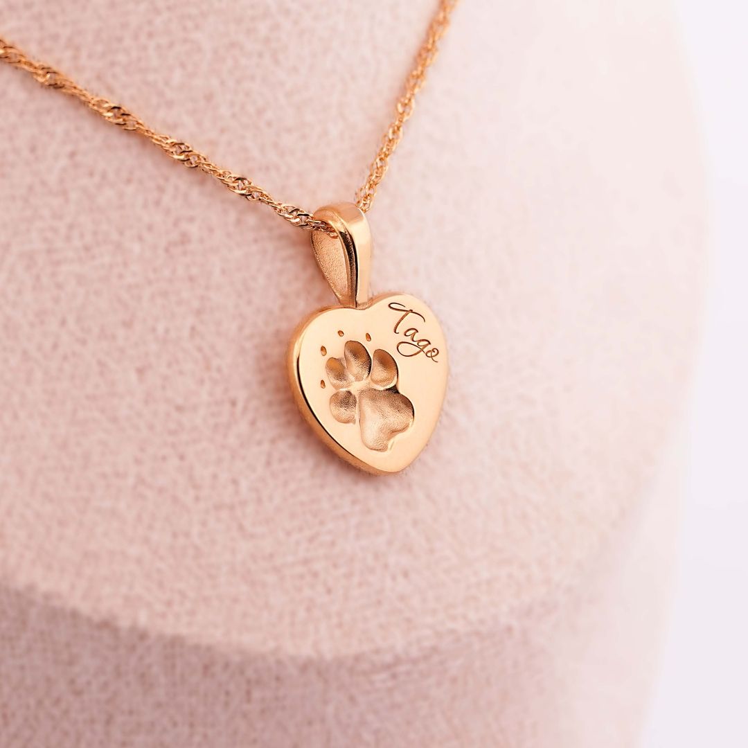 Goldene Halskette mit herzförmigem Anhänger, eingravierte Pfote und Name Tayo, auf beigem Schmuckdisplay