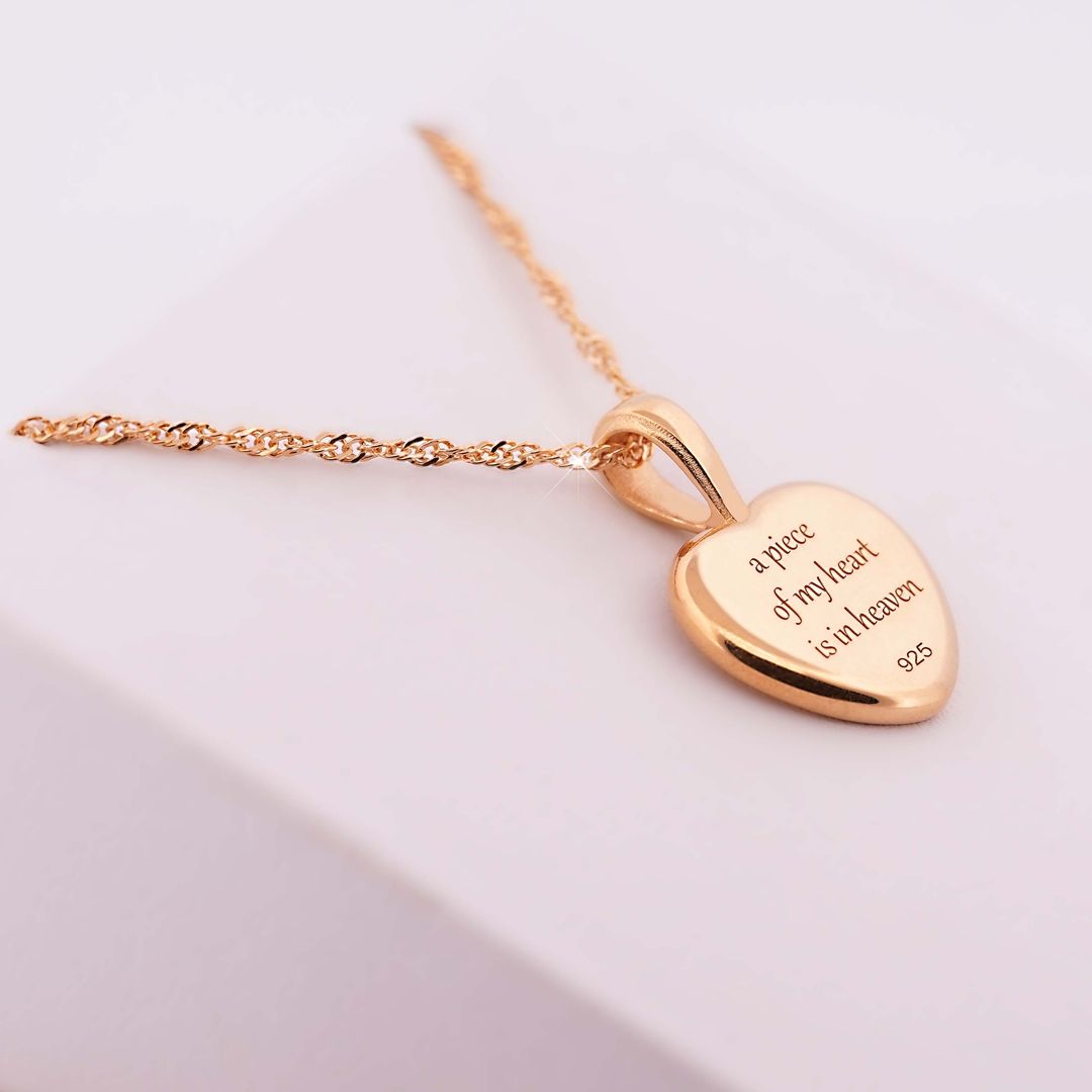 Goldene Halskette mit herzförmigem Anhänger, Gravur a piece of my heart is in heaven, auf heller Unterlage