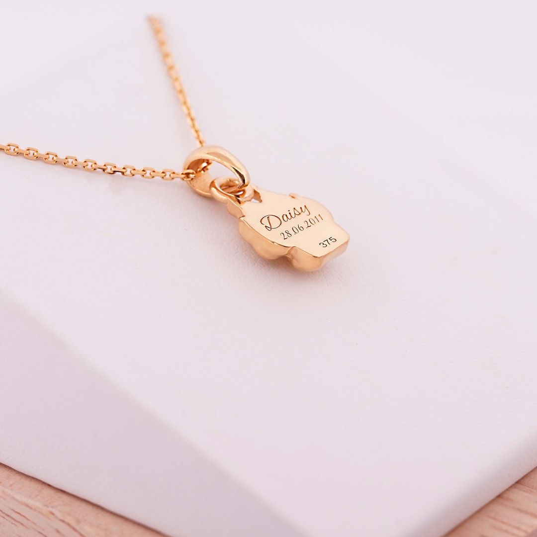 Goldene Halskette mit graviertem Anhänger in Pfotenform, Gravur Daisy 28.06.2011, auf heller Unterlage